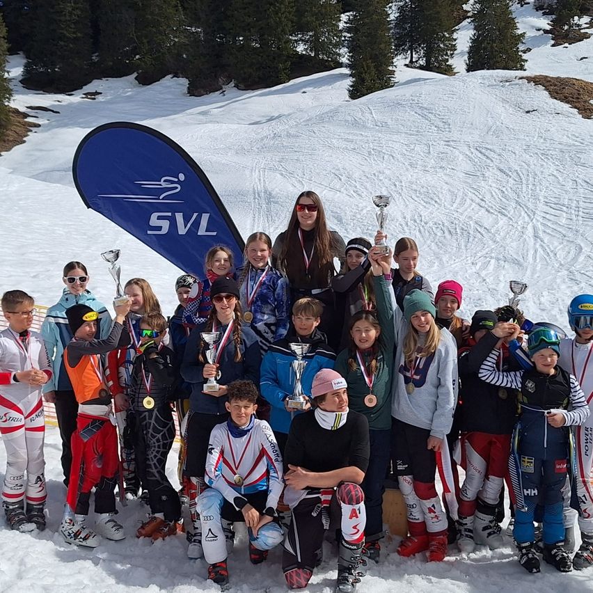 Eine Gruppe von Skifahrern posiert im Schnee mit ihren Medaillen und Trophäen für ein Foto.