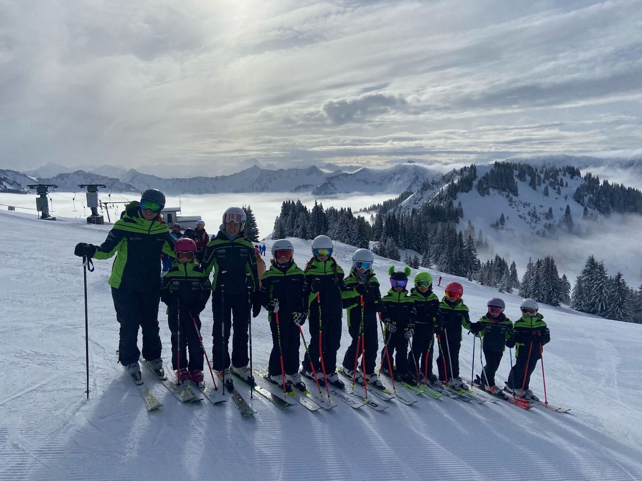 Eine Gruppe junger Skifahrer, die grüne und schwarze Skianzüge tragen, posiert für ein Foto auf einem verschneiten Berg.