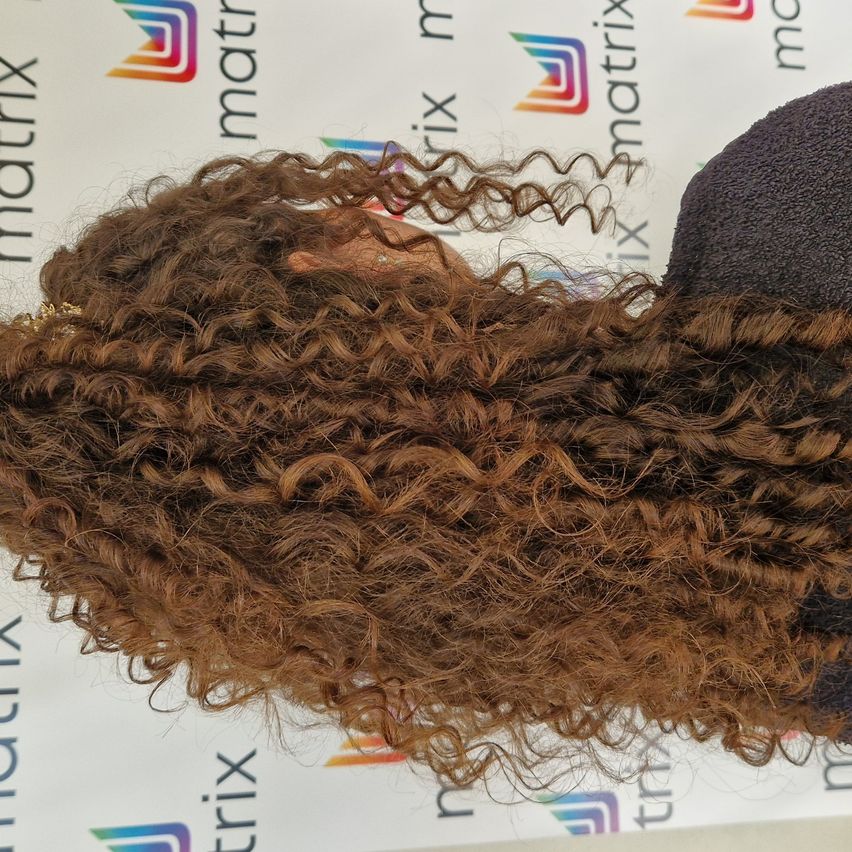 Eine Nahaufnahme von braunem, lockigem Haar, das locker in einer Kaskade fällt, vor einem Hintergrund mit Logos und Text.