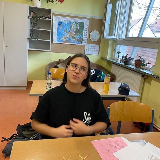 Bild enthält, Furniture, Table, Person, Face, Head, Text, Desk, Student, Plant