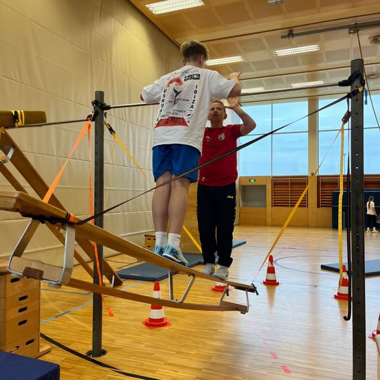 Bild enthält, Wood, Person, Clothing, Shorts, Floor, Flooring, Footwear, Shoe, Gymnastics, Face