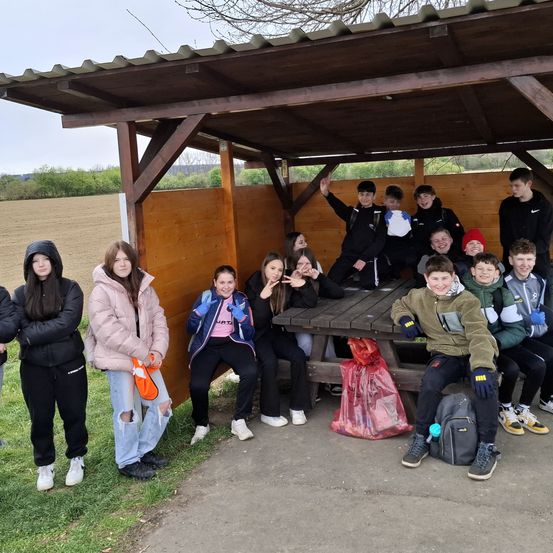 Eine Gruppe von Teenagern posiert für ein Foto in einem hölzernen Unterstand mit einer Holzbank in einem Grasbereich.