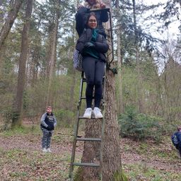 Eine Frau klettert eine Leiter an einem Baum hoch, während ein Mann an ihr festhält.