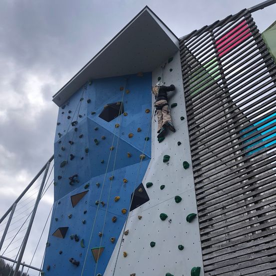 Eine Person klettert an einer Indoor-Kletterwand mit farbenfrohen geometrischen Designs an der Seite.