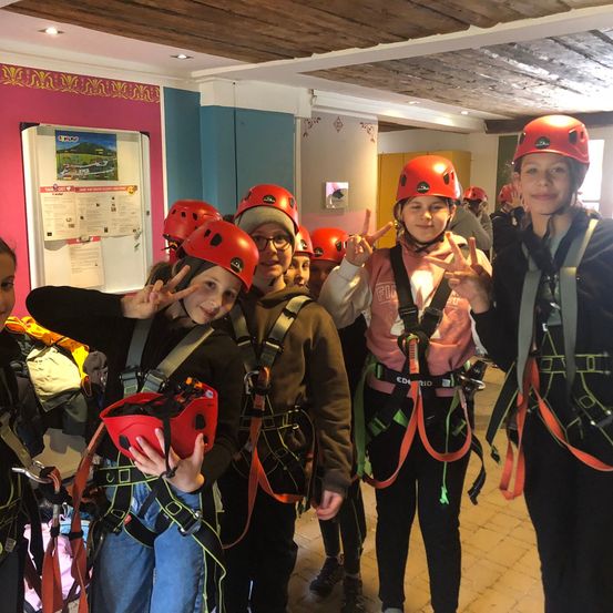 Eine Gruppe von Kindern mit roten Helmen steht in einem Raum. Sie lächeln und machen Friedenszeichen mit den Händen.