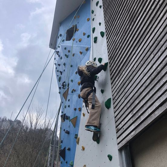 Eine Person klettert an einer Kletterwand an der Seite eines Gebäudes.