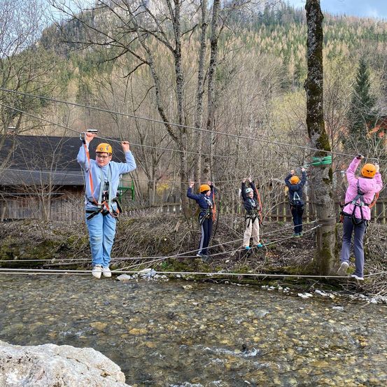 Eine Gruppe von Menschen mit Helmen steht auf einer Seilbahn über einem Fluss.