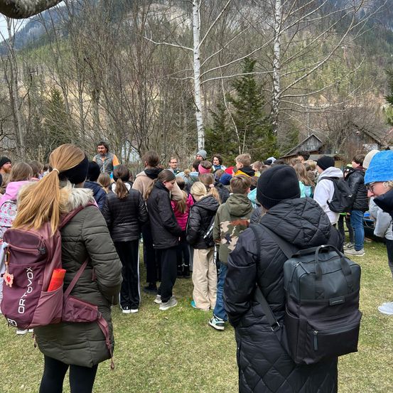 Eine Gruppe von Menschen steht in einer Reihe auf einem Grasfeld mit Bäumen im Hintergrund.