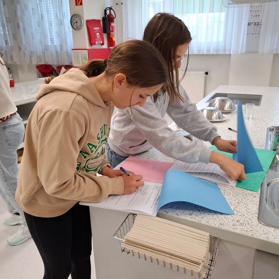 Zwei junge Frauen schreiben mit blauen Markern auf Papier auf einer Küchentheke.