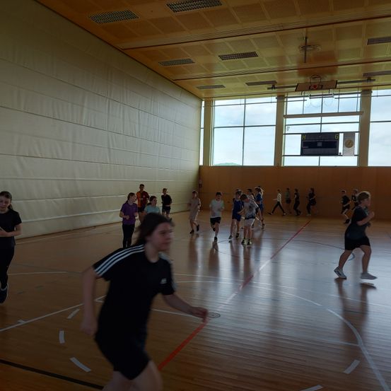 Mehrere Kinder laufen auf einem Basketballplatz mit Holzboden. Sie tragen Sportbekleidung und Turnschuhe.