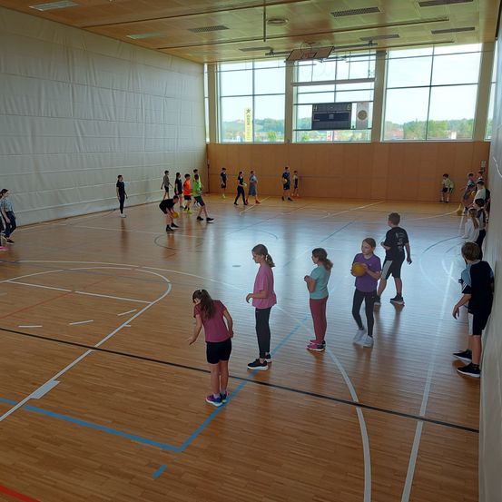 Ein Hallenbasketballfeld mit Kindern, die Ballspiele spielen. Mehrere Kinder stehen und spielen Basketball.