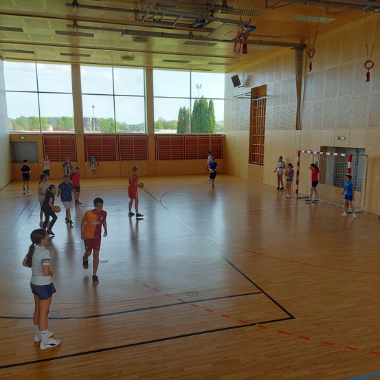 Eine Gruppe von Kindern spielt Basketball in einer Turnhalle. Einige von ihnen rennen, während andere stehen und einen Basketball halten.