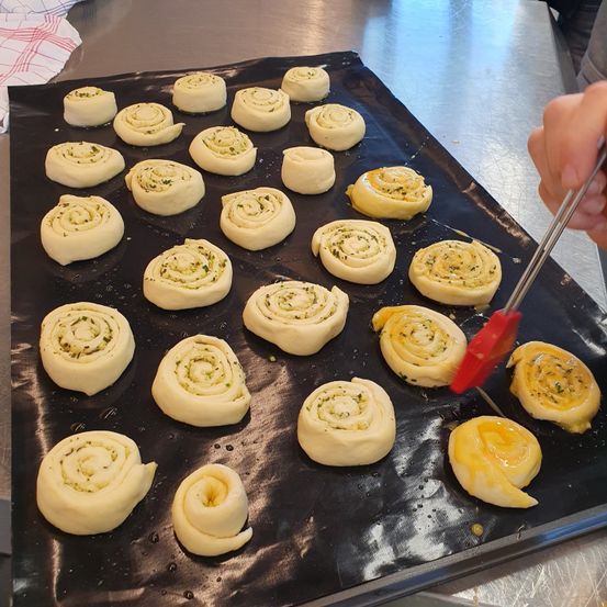 Ein Tablett mit Teigrollen, wobei eine Person einen roten Pinsel verwendet, um eine Ei-Waschung auf die Oberseite einer Rolle aufzutragen.