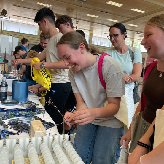 Eine Gruppe von Menschen ist in einem Gebäude. Ein Mädchen lächelt und scheint etwas zu reparieren. Ein Mann hält eine gelbe Tasche. Eine Frau steht hinter ihnen.