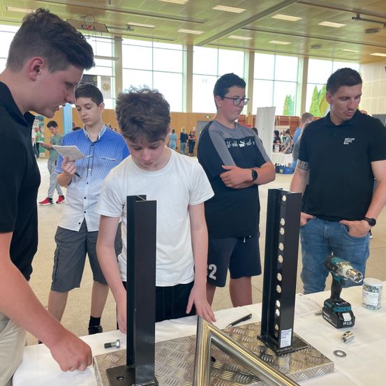 Eine Gruppe junger Männer arbeitet in einer Halle an einem Projekt. Ein Mann bohrt mit einem Akkuschrauber.