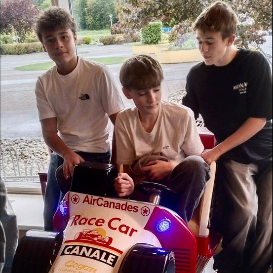 Drei Jungen stehen vor einer Fahrt, Air Canada Race Car, wobei einer der Jungen das Lenkrad hält.