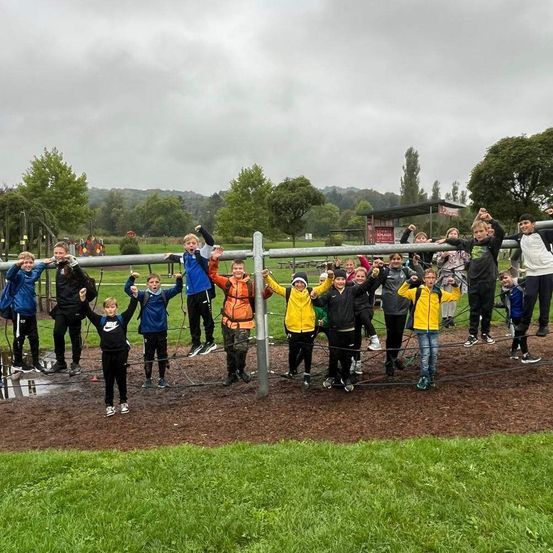 Eine Gruppe von Kindern spielt und posiert für ein Foto auf einem Spielplatz bei bewölktem Himmel.
