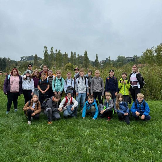Eine Gruppe von Schülern und Lehrern posiert für ein Gruppenfoto auf einem Rasenfeld mit Bäumen im Hintergrund.