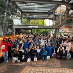 Eine Gruppe von Kindern und Erwachsenen posiert vor einem modernen Gebäude für ein Foto, einige halten Geschenktüten.