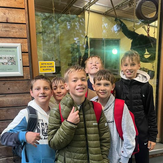 Eine Gruppe junger Jungen posiert für ein Foto vor einem Gebäude mit einem Affen im Inneren. Sie lächeln und scheinen für ein Foto zu posieren.