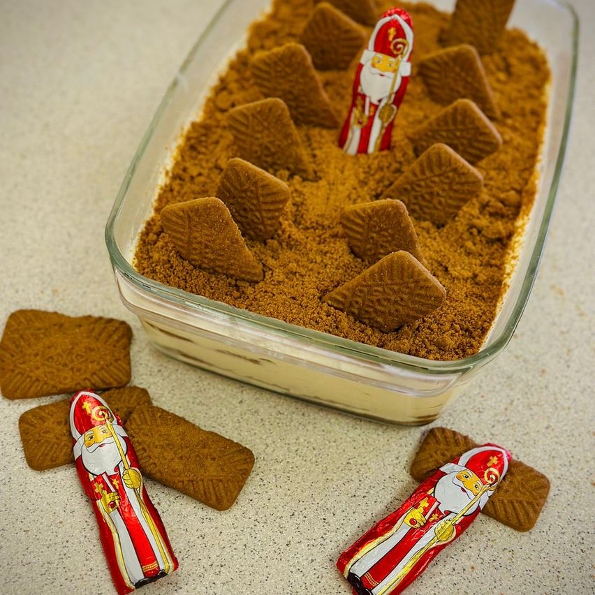 Eine Glasschale mit einer cremigen Nachspeise gefüllt, die mit braunem Pulver bestreut und mit kleinen Nikolaus-Keksen und -Figuren verziert ist.