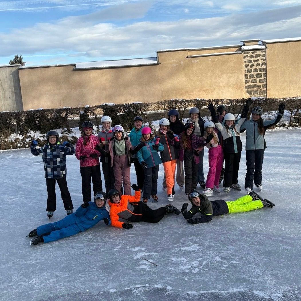 A group of people in winter gear pose for a photo on an icy surface with a building in the background.