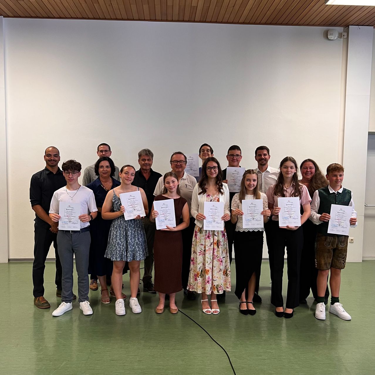 Gruppenfoto von Menschen, die Urkunden halten, stehen in einem Raum und lächeln für ein Foto.