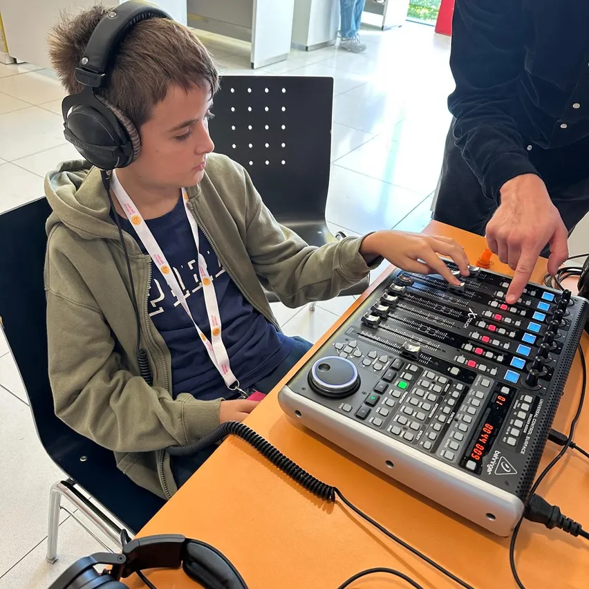 Ein junger Junge mit Kopfhörern bedient eine Soundmischkonsole, während eine Person hinter ihm steht.