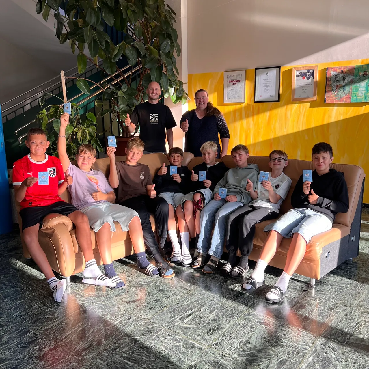 Eine Gruppe von Jungen und einer Frau, die auf einer Couch sitzen, Karten hochhalten und lächeln.