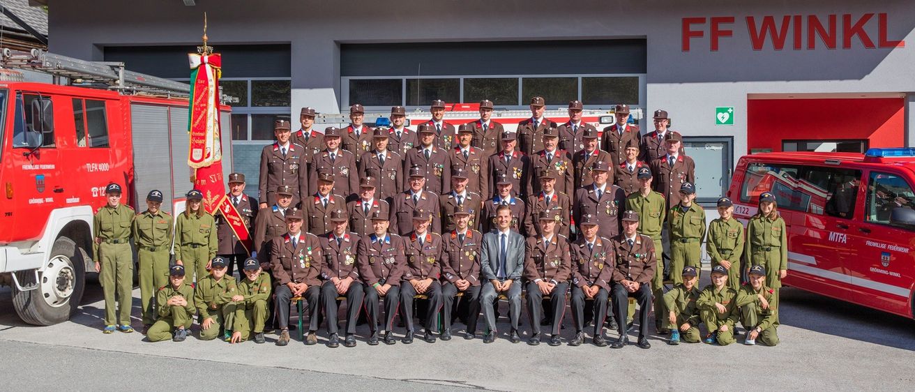 Eine Gruppe Feuerwehrleute in Uniform posiert für ein Foto vor einer Feuerwache.