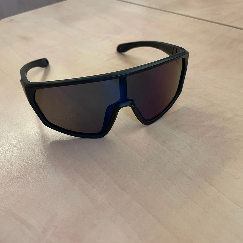 Ein Paar schwarze Sonnenbrille mit dunklen Gläsern und einem schlanken Rahmen liegt auf einem Holztisch.