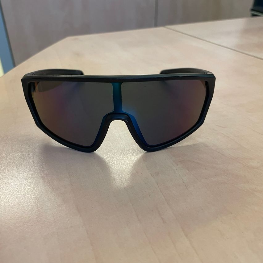 Ein Paar schwarze Sonnenbrille mit blauen Rahmen und dunklen Gläsern liegt auf einem Holztisch.