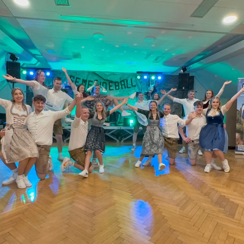 Eine Gruppe von Menschen in traditioneller Kleidung posiert für ein Foto auf einem hölzernen Tanzboden mit bunten Lichtern.