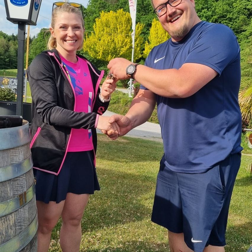 A woman in a pink shirt and a man in a blue shirt are shaking hands, possibly at an event.