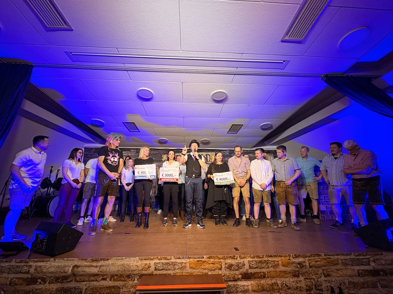 A group of people stand on a stage with a microphone, holding up signs with prize amounts, possibly at an awards ceremony.