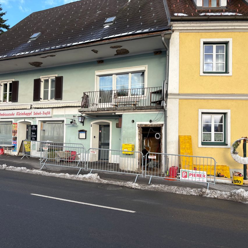 A building with a balcony and a store on the ground floor. A closed sign is displayed. Metal barriers and a signboard are placed in front of the building. Snow is on the ground.