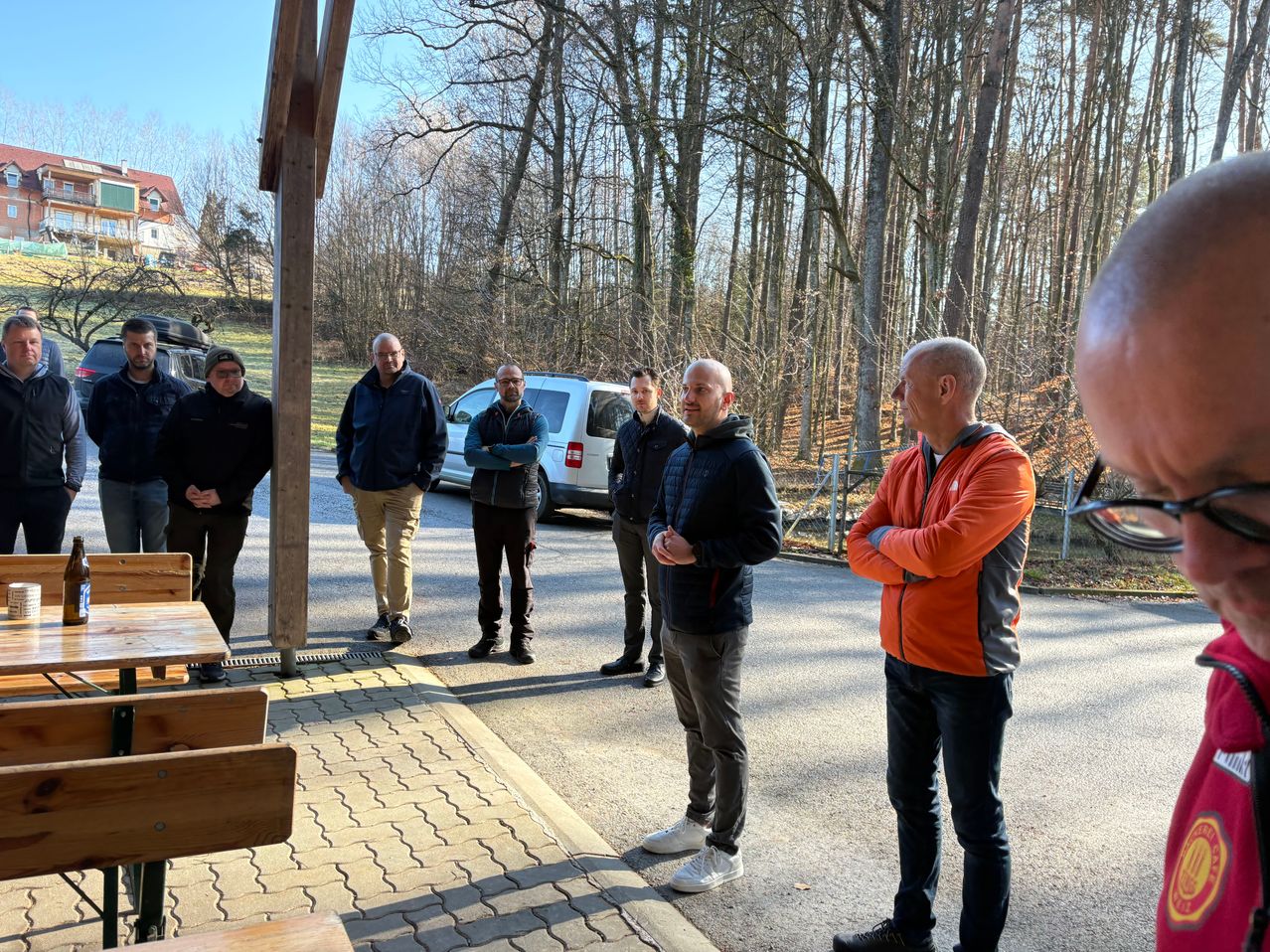 Eine Gruppe von Männern steht auf einem Parkplatz mit einem weißen Van und einem Haus im Hintergrund.