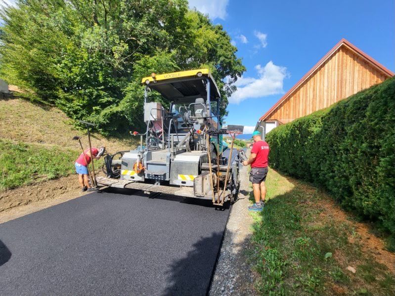 Zwei Arbeiter verwenden eine Straßenasphaltmaschine, um neuen Asphalt auf einer Straße zu verlegen. Einer führt die Maschine, während der andere die Oberfläche glättet.