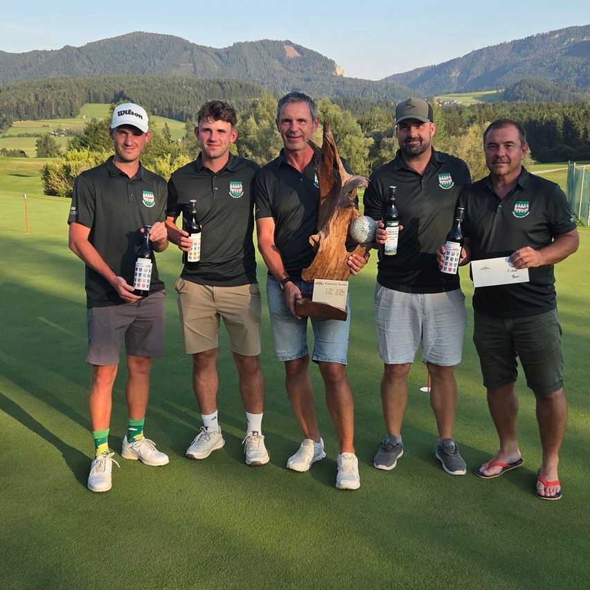 Five men in matching black polo shirts stand on a golf course, holding bottles of beer and a trophy. They are smiling and posing for a photo.