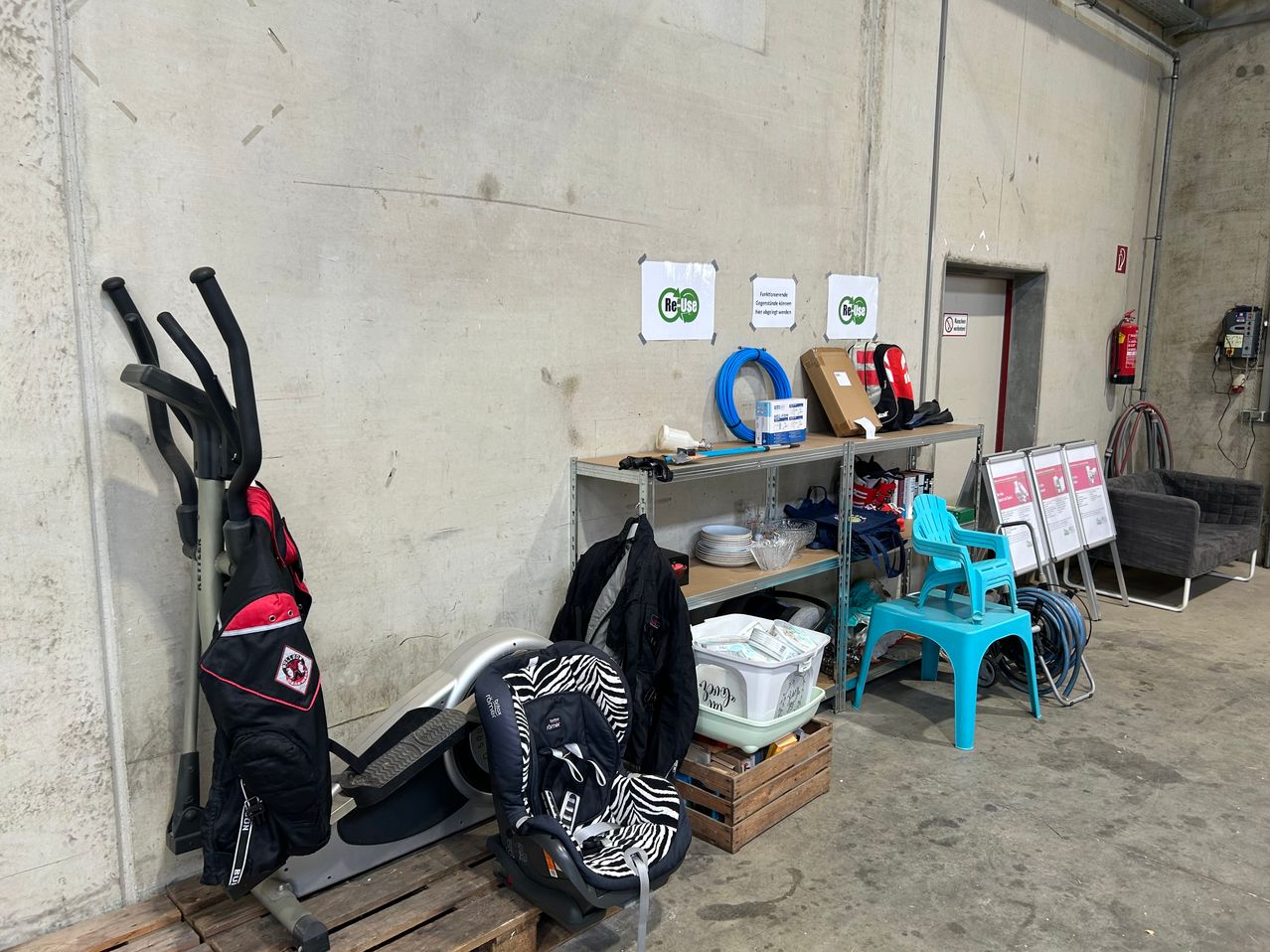 A storage area with various items including a baby car seat, exercise equipment, and storage boxes. A shelf holds plates, bowls, and a box. A sign on the wall reads 'ReUse'.
