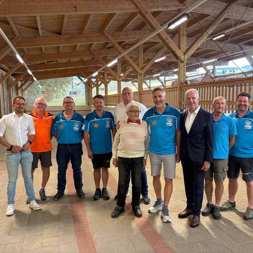 Eine Gruppe von Menschen steht in einem Raum, trägt blaue T-Shirts und schwarze Shorts. Sie posieren für ein Foto.