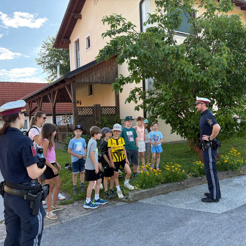 A police officer speaks to a group of children in front of a house. The children are dressed in casual clothes.