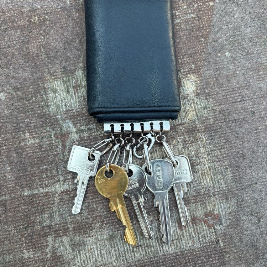 A collection of assorted keys on a leather keychain with a silver clasp, placed on a wooden surface.