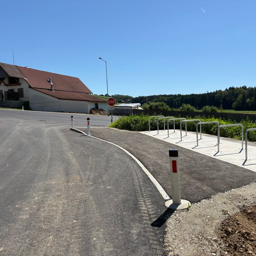 An empty road with a stop sign, a building, a sidewalk with bike racks, and a clear blue sky.