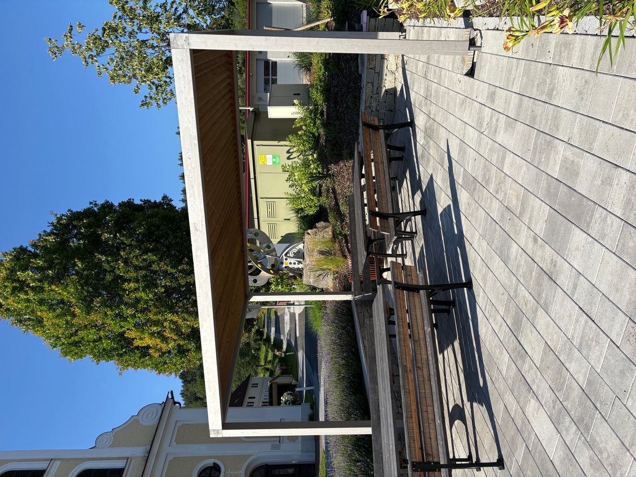 Atop a wooden deck, an outdoor seating area with a canopy and benches is visible. Trees and a building are in the background.