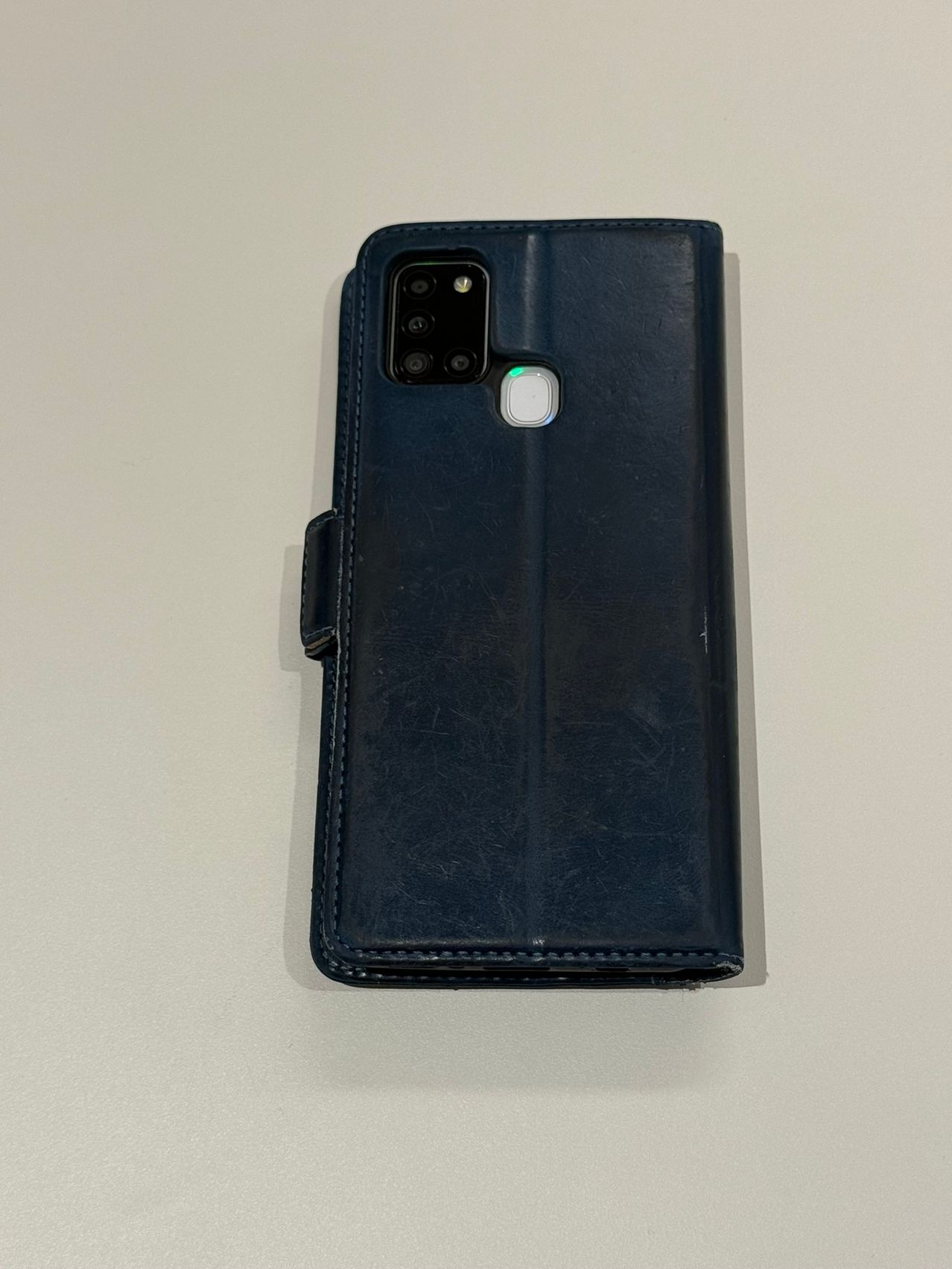 The back of a navy blue leather-like phone case with a camera module and a flash is displayed on a white surface.