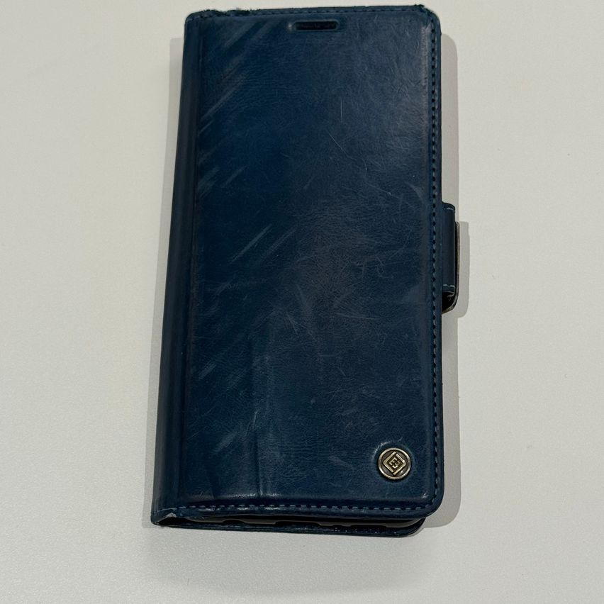 A navy blue leather case for a phone, with a silver logo, is displayed on a white surface.
