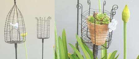 Drei metallische Pflanzenständer mit gelben Blumen und einer Pflanze in einem braunen Topf. Ein Ständer hat einen Drahtkäfig, der einem Vogelkäfig ähnelt.