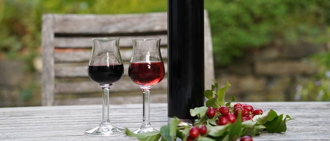 Eine Flasche mit dunkler roter Flüssigkeit und zwei kleinen Gläsern derselben Flüssigkeit auf einem Holztisch mit roten Beeren und Blättern.