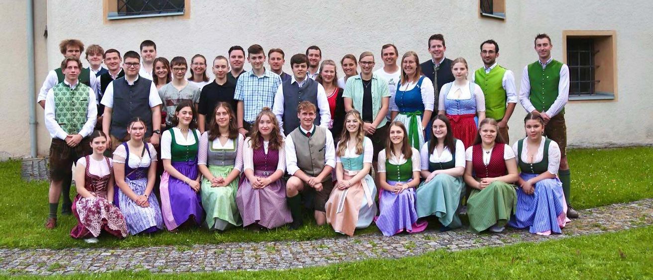 Eine Gruppe von Menschen in traditioneller Kleidung posiert für ein Foto vor einem Gebäude mit Bogenfenstern.